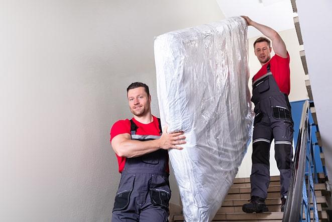 two people carrying a box spring down a staircase in East Windsor